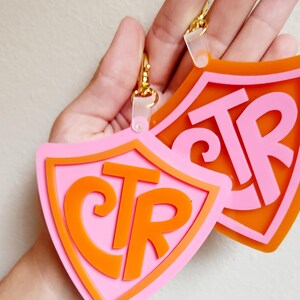 May include: Two pink and orange shield-shaped keychains with the letters "CTR" in a stylized font.
