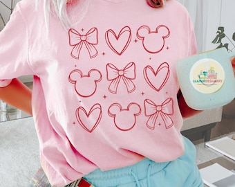 May include: Pink t-shirt with a red graphic design of hearts, bows, and Mickey Mouse heads.