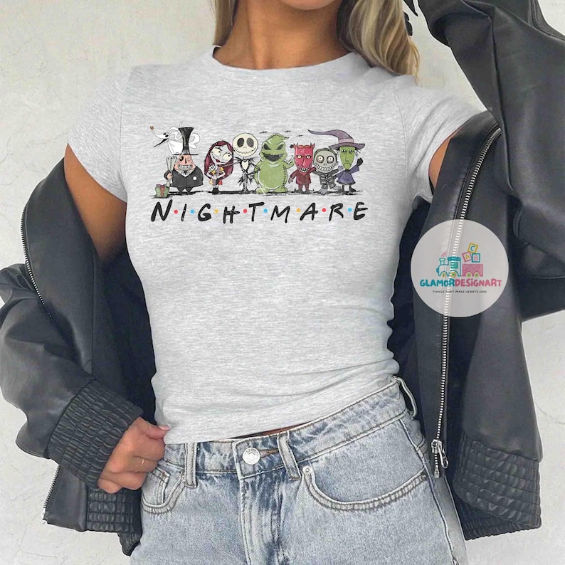 Może przedstawiać: Jasnoszara koszulka z kresk&oacute;wkową grafiką postaci z "Miasteczka Halloween" i napisem "NIGHTMARE". Koszulka ma kr&oacute;tkie rękawy.