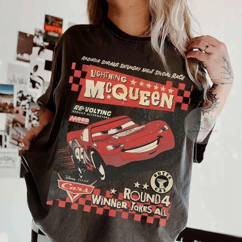 Może przedstawiać: Ciemnoszara koszulka z Lightning McQueen z filmu Disney Pixar Cars. Grafika zawiera tekst "Radiator Springs Saturday Night Special Race" i "Winner Takes All". Projekt jest w kolorach czerwonym, białym i czarnym.