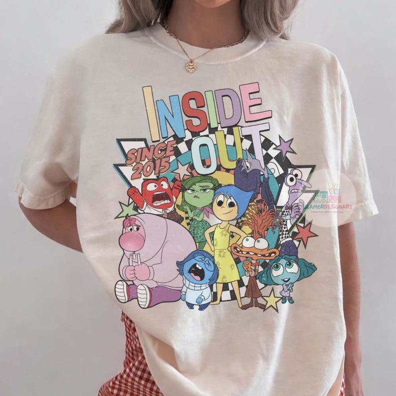 Pu&ograve; includere: T-shirt color crema con le parole "INSIDE OUT" in lettere colorate, il testo "SINCE 2015" e vari personaggi dei cartoni animati del film. Il design include stelle e un motivo a scacchi.