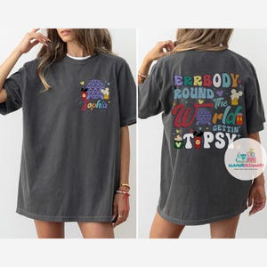 May include: A gray t-shirt with a colorful graphic on the front and back. The front graphic features a cartoon Mickey Mouse, a Spaceship Earth, and a beer mug. The back graphic features the text "Everybody Round the World Gettin' Tipsy" with a cartoon Mickey Mouse, a Spaceship Earth, and a beer mug.