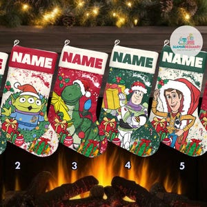May include: Five Christmas stockings featuring different Toy Story characters. The stockings are red, green and white with a snowy background. The characters are Woody, Buzz Lightyear, Rex and a green alien. The stockings have the word "NAME" written on them.