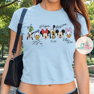 Puede incluir: Camiseta azul claro recortada con un gr&aacute;fico de Mickey Mouse, Minnie Mouse, Donald Duck, Goofy, Pluto y Daisy Duck. El gr&aacute;fico incluye los nombres y las firmas de los personajes.