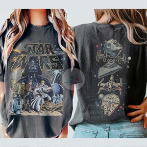 May include: Dark gray Star Wars t-shirt featuring Darth Vader, Luke Skywalker, and other characters. The front of the shirt displays the Star Wars logo. The back of the shirt has illustrations of the Death Star, a Star Destroyer, X-wing, and the Millennium Falcon.