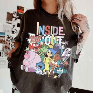 Pu&ograve; includere: T-shirt nera con un design del film "Inside Out". Il design include le parole "INSIDE OUT" a colori, il testo "SINCE 2015" e personaggi dei cartoni animati. La maglietta ha un aspetto vintage e sbiadito.