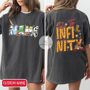 Puede incluir: Una camiseta gris oscuro con un nombre personalizado escrito en personajes de dibujos animados coloridos de la pel&iacute;cula Toy Story. La parte posterior de la camiseta tiene el texto "To Infinity and Beyond" en cuerda amarilla con un personaje de dibujos animados de la pel&iacute;cula.