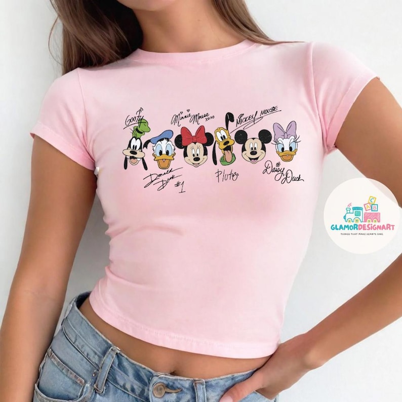 Puede incluir: Camiseta rosa de manga corta y corte corto con un estampado gr&aacute;fico de Mickey Mouse, Minnie Mouse, Donald Duck, Goofy, Pluto y Daisy Duck. Los personajes est&aacute;n en fila con sus nombres escritos debajo.