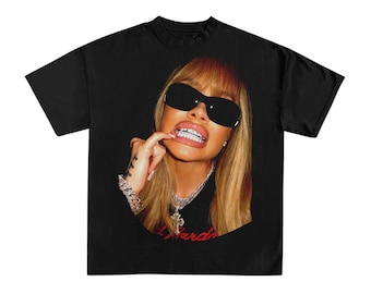 Peut inclure: T-shirt noir avec une image en gros plan d'une personne portant des lunettes de soleil et une chaîne en argent. La personne touche ses dents, qui ont des broches argentées. Le mot "Hard" est visible en script rouge.