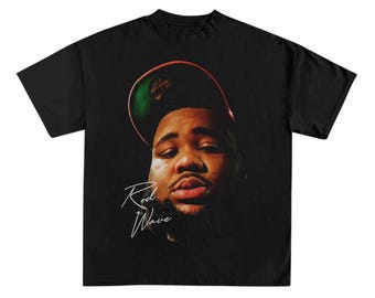 May include: Black t-shirt with a graphic of a man wearing a green and red baseball cap. The man's face is visible and the text "Rod Wave" is written in white below the graphic.
