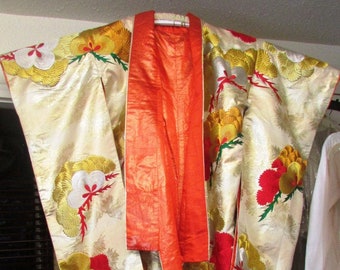 May include: A traditional Japanese kimono with gold and red embroidery. The kimono is made of a white silk fabric and has a long, flowing design. The kimono is decorated with floral patterns and has a red sash.