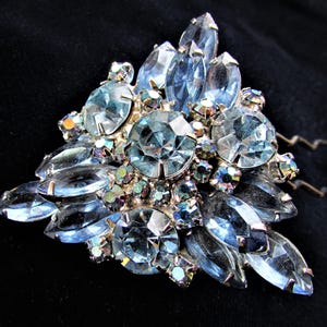 Puede incluir: Un peine para el cabello vintage con un grupo de diamantes de imitación de color azul claro y transparente. El peine está hecho de metal y tiene dos púas.