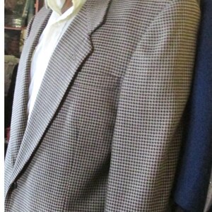 May include: A brown and black houndstooth blazer with a white collared shirt underneath. The blazer has a two-button closure and a pocket on the left side. The mannequin is wearing the blazer.