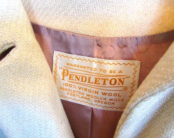 Puede incluir: Un abrigo de lana blanco con forro marrón y una etiqueta blanca que dice "WARRANTED TO BE A PENDLETON' 100% VIRGIN WOOL PENDLETON WOOLEN MILLS PORTLAND, OREGON"