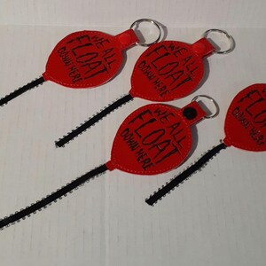 May include: Four red balloon-shaped keychains with black ribbon loops and silver key rings. Each keychain features the text "We All Float Down Here".