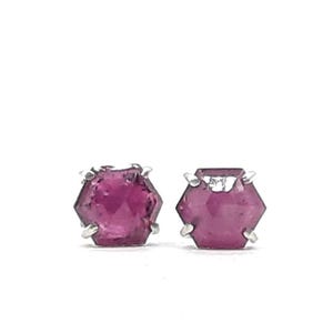 Peut inclure: Une paire de boucles d'oreilles à clous avec des pierres précieuses hexagonales rose foncé serties d'argent. Les pierres précieuses ont un aspect facetté, captant la lumière. Les boucles d'oreilles sont présentées sur fond blanc.