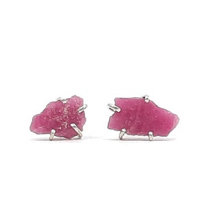 May include: A pair of silver stud earrings featuring raw pink gemstones. The gemstones are irregular in shape and have a natural, rough texture.