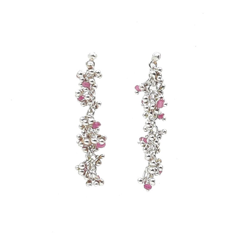 Pu&ograve; includere: Un paio di orecchini pendenti color argento. Ogni orecchino presenta un design a grappolo con piccole perle rotonde argentate e pietre preziose rosa. Gli orecchini pendono verticalmente, creando un aspetto delicato ed elegante.