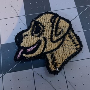 May include: A yellow embroidered patch of a dog's head with a pink tongue sticking out.