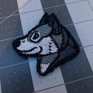 Peut inclure: Patch brodé représentant la tête d'un husky gris et blanc avec un contour noir. Le patch est conçu pour être cousu sur des vêtements ou des sacs.