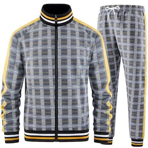 Puede incluir: Un chándal a cuadros grises con chaqueta y pantalón a juego. La chaqueta tiene cremallera frontal, cuello negro con rayas amarillas y blancas y rayas amarillas en las mangas. Los pantalones tienen cintura con cordón y rayas amarillas en los laterales.