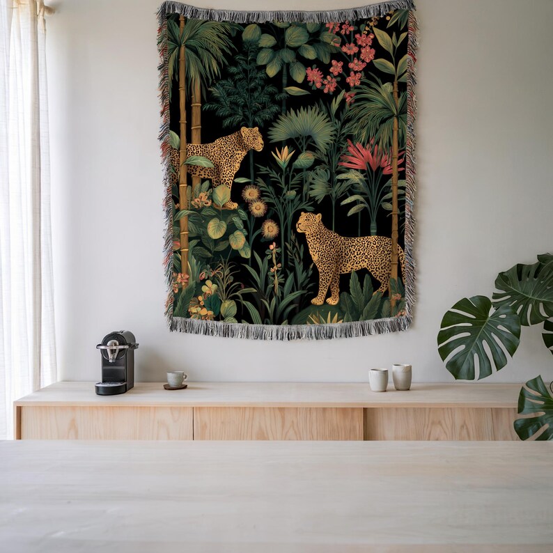 May include: A woven tapestry featuring a jungle scene with two leopards amidst lush greenery and flowers. The background is black, and the tapestry has a fringed edge. The leopards have a spotted pattern, and the plants are in shades of green, yellow, and pink.