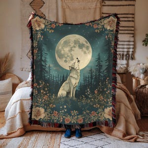 May include: A woven throw blanket featuring a wolf howling at a full moon in a forest setting. The blanket has a dark teal background with floral accents and a fringed edge. The wolf is white, and the moon is bright.