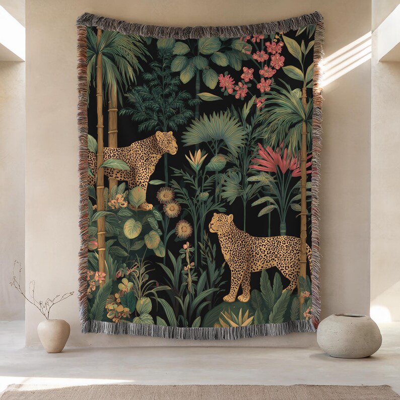 May include: A woven tapestry featuring a jungle scene with two leopards amidst lush greenery and pink flowers against a black background. The tapestry has a fringed edge and is designed for wall hanging.