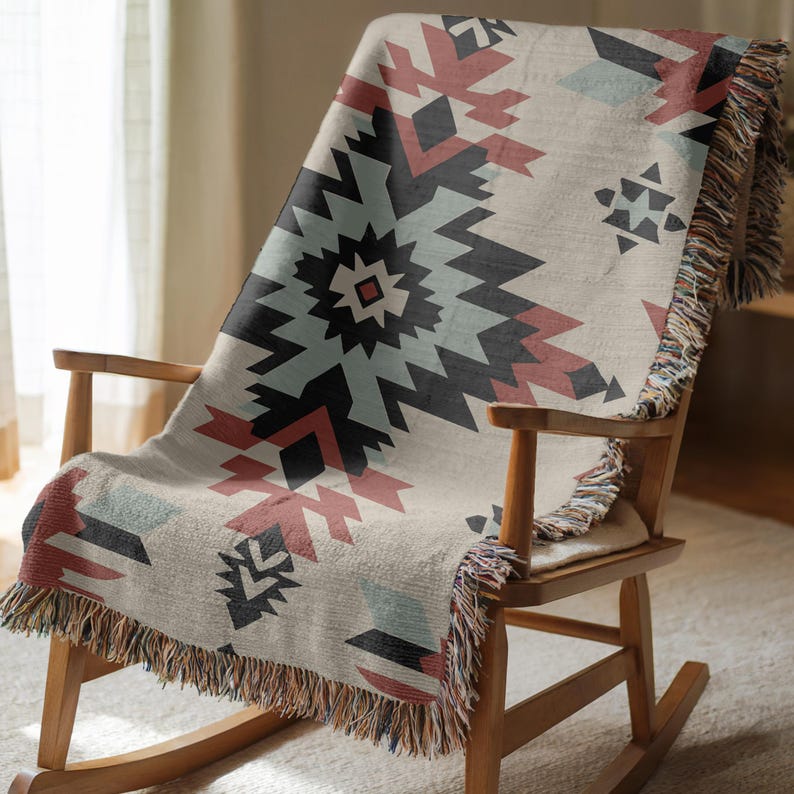 Pu&ograve; includere: Una coperta tessuta con un motivo geometrico nei toni del nero, rosso spento e azzurro su fondo crema. La coperta presenta una superficie testurizzata e frange decorative lungo i bordi, drappeggiata su una sedia a dondolo in legno.
