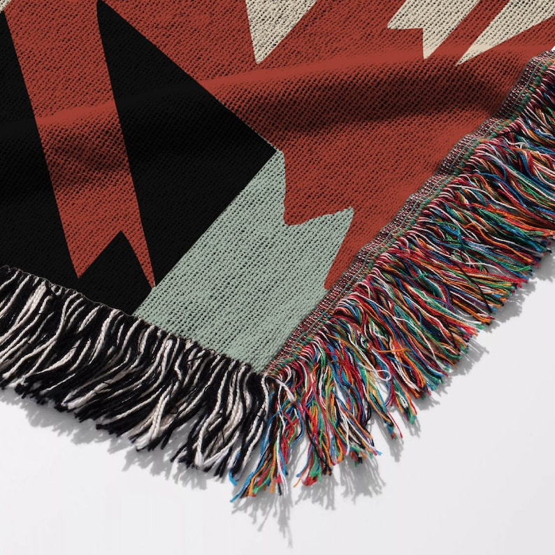 Pu&ograve; includere: Una coperta tessuta con un motivo geometrico nei colori terracotta, nero e crema. Il tessuto presenta una trama strutturata ed &egrave; rifinito con un bordo a frange decorativo che mostra un vivace mix di fili multicolori lungo il perimetro.