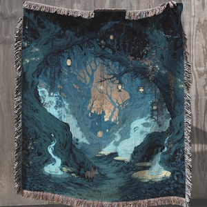 May include: A woven throw blanket featuring a dark forest scene with deep blue and teal tones. The design includes glowing lanterns hanging from twisted tree branches, a small fox near the base, and a central structure illuminated by warm light.