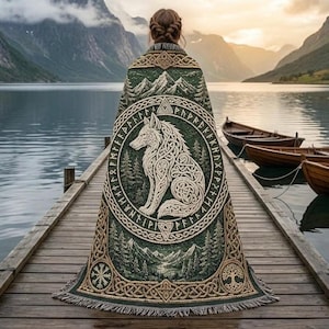 Könnte beinhalten: Eine grüne Webdecke mit einer zentralen cremefarbenen Wolfsillustration in einem kreisförmigen Rahmen mit Runensymbolen. Das Design umfasst Berg- und Waldmotive, komplizierte keltische Knotenmuster und einen unteren Rand mit Fransen.
