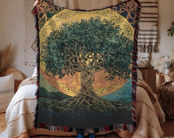 May include: A woven tapestry blanket featuring a detailed illustration of a tree with intertwined roots and branches. The tree is set against a golden circular background with Celtic knotwork. The blanket has a fringed edge with red and black accents.