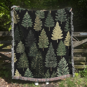 May include: A black woven throw blanket with a repeating pattern of green and yellow trees. The blanket has a fringe border.