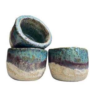 Puede incluir: Tres cuencos de cerámica hechos a mano con un esmalte único. Los cuencos presentan una mezcla de colores, incluyendo turquesa, marrón y beige. La superficie texturizada se suma a la estética rústica. Estos cuencos son ideales para servir o como piezas decorativas.