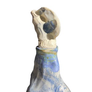 Puede incluir: Un tapón de botella de cerámica hecho a mano con un diseño abstracto único. El tapón presenta una parte superior beige claro, con forma de calavera, con un interior azul, sobre una base veteada azul y blanca. Artículo decorativo.