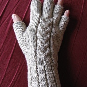 May include: A pair of beige fingerless gloves with a cable knit pattern. The gloves are knitted in a fine gauge yarn and have a ribbed cuff.