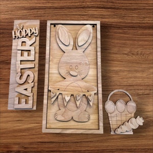 May include: Wooden Easter decorations with a bunny holding a banner with hearts, a basket with eggs, and a sign that says "Hoppy Easter".
