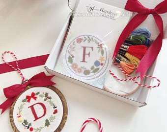 May include: A Christmas-themed embroidery kit with a wooden hoop ornament featuring the letter "D" and a red bow. The kit includes embroidery floss, a round patch with the letter "F", and a candy cane.