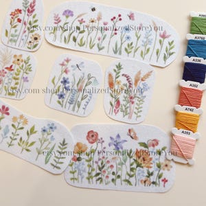 May include: A collection of embroidered patches featuring colorful floral designs, including wildflowers and butterflies. The patches are in various shapes and sizes, with a white background. Spools of embroidery thread in various colors are also visible.