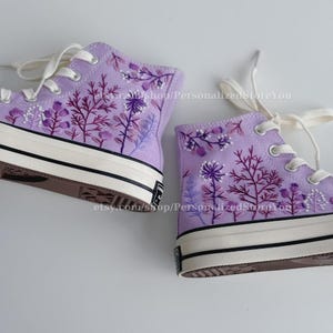 Könnte beinhalten: Lilafarbene High-Top-Canvas-Sneaker mit gestickten Blumenmustern. Die Blumen sind in Violett-, Rosa- und Weißtönen gehalten.