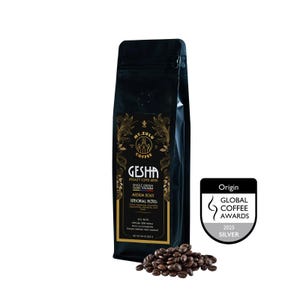 May include: A black coffee bag labelled Mt. Zulu Coffee Gesha Specialty Coffee Beans, Medium Roast, from Caldas, Colombia. The label lists sensorial notes, SCA 86.75+, 1800 metres altitude, and net weight 250 g. A pile of coffee beans sits nearby.