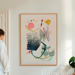 Può includere: Stampa d'arte astratta in una cornice di legno naturale. L'opera presenta forme e linee colorate in rosa, blu, giallo e verde. Un piccolo sgabello in legno sostiene libri e una pianta in vaso. Una persona vestita di bianco passa.