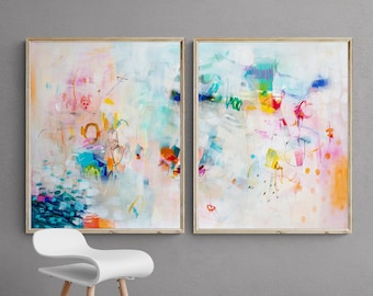 Può includere: Due dipinti astratti in cornici bianche con uno sgabello bianco davanti a un muro grigio. I dipinti sono entrambi astratti e presentano una varietà di colori, tra cui rosa, blu, giallo e verde. I dipinti sono entrambi in stile moderno.
