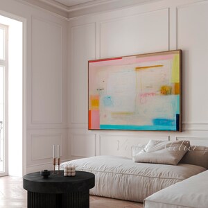 Puede incluir: Pintura abstracta con colores rosa, azul, amarillo y naranja sobre fondo blanco. La pintura est&aacute; colgada en una pared blanca sobre un sof&aacute; blanco y una mesa de caf&eacute; negra.
