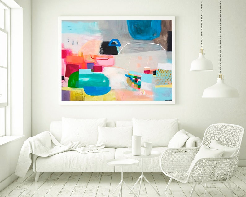 Op de afbeelding: Abstract schilderij met een witte achtergrond en kleurrijke geometrische vormen in tinten roze, blauw, groen en geel. Het schilderij is ingelijst in een wit frame en hangt aan een witte muur.