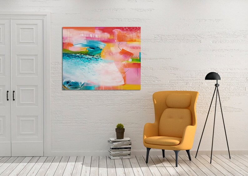May include: Abstract painting with bright colors, including pink, blue, green, and yellow. The painting is hanging on a white wall in a room with a yellow armchair and a black tripod lamp.