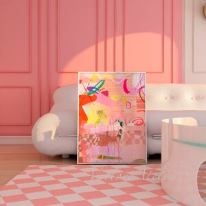 Op de afbeelding: Abstracte kunstprint met roze, gele, oranje, groene en blauwe kleuren. De print is ingelijst en hangt aan een roze muur boven een witte bank.