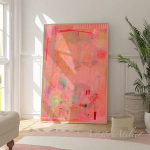 May include: Large abstract art print in shades of pink, orange, and green. The artwork is displayed in a light wood frame and leans against a white wall. The room features a window, a plant, and a rug.