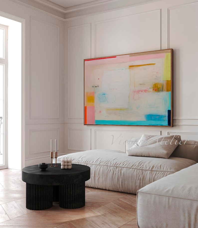 Puede incluir: Pintura abstracta con colores rosa, azul, amarillo y naranja sobre fondo blanco. La pintura est&aacute; colgada en una pared blanca sobre un sof&aacute; blanco y una mesa de caf&eacute; negra.
